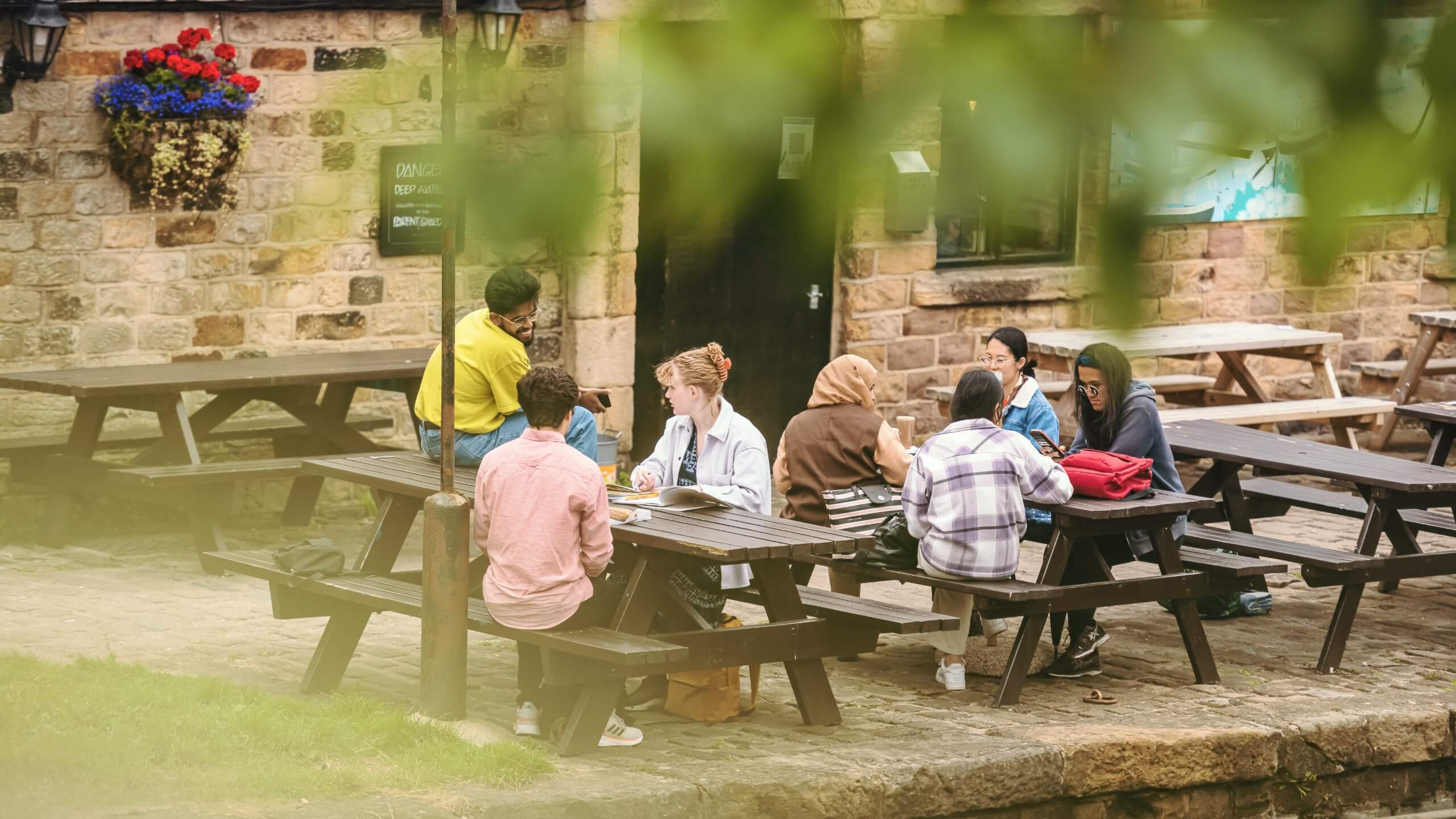 Two groups of students sit on picnic benches outside a pub on the canal.