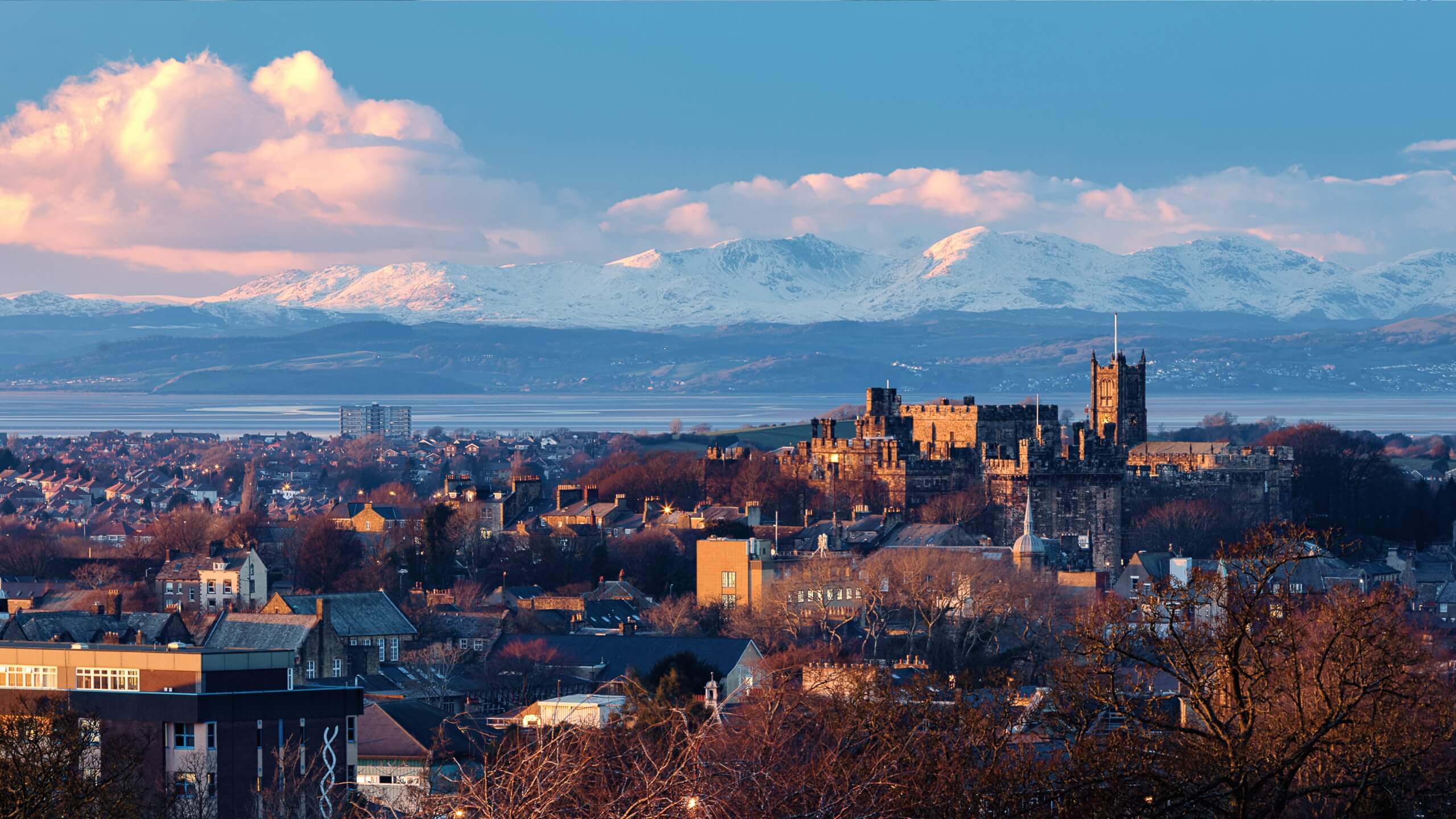 A winter landscape photo of the Lancaster skyline with snowy Lake District fells in the background