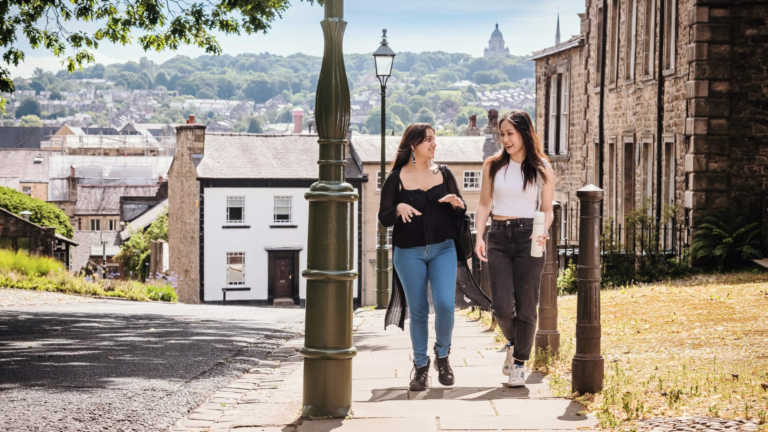Two students walk in Lancaster's historic streets near the castle. The Ashton Memorial is on the top of the hill in the background.