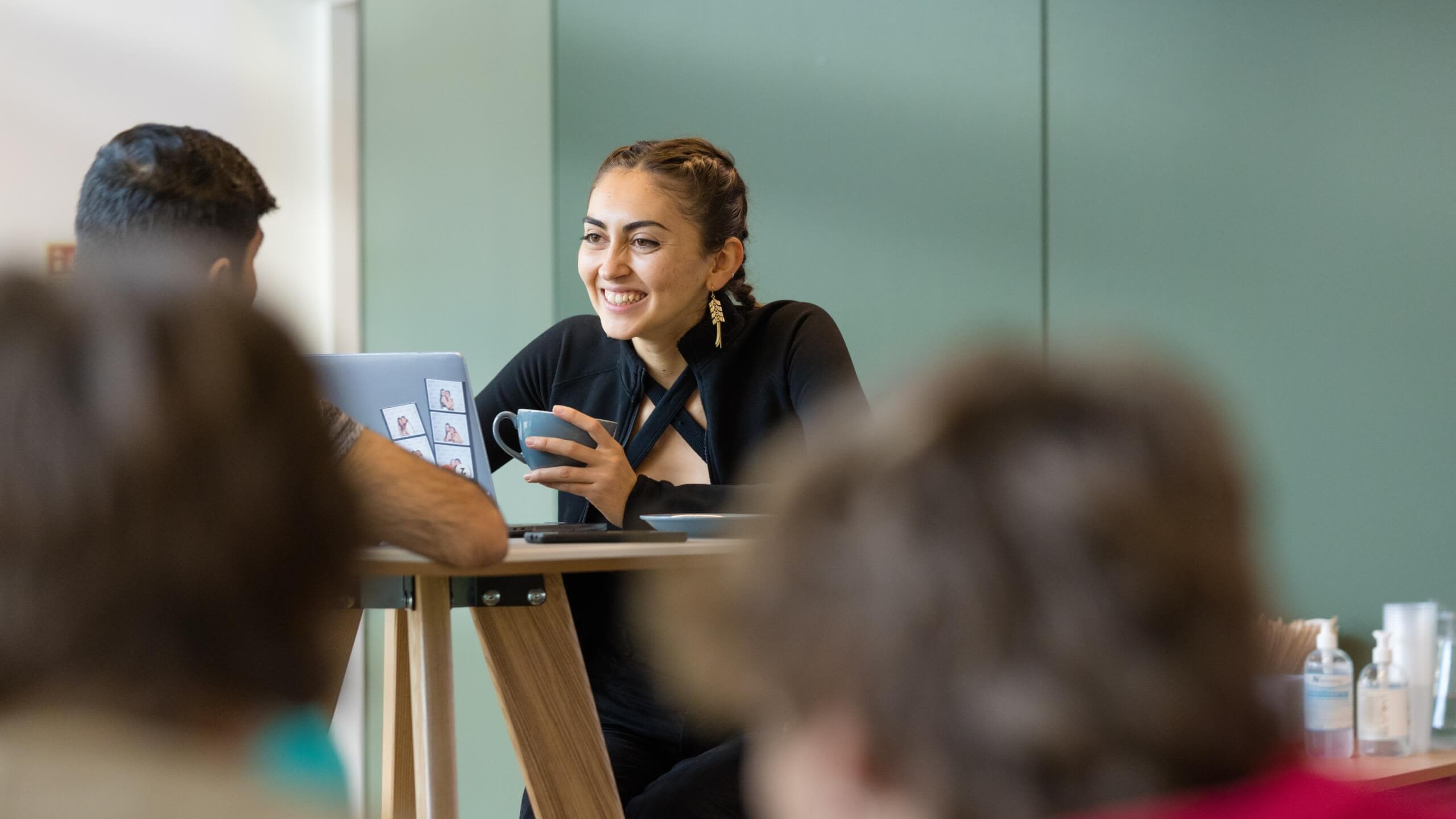A student holds a coffee cup and laughs with her friend