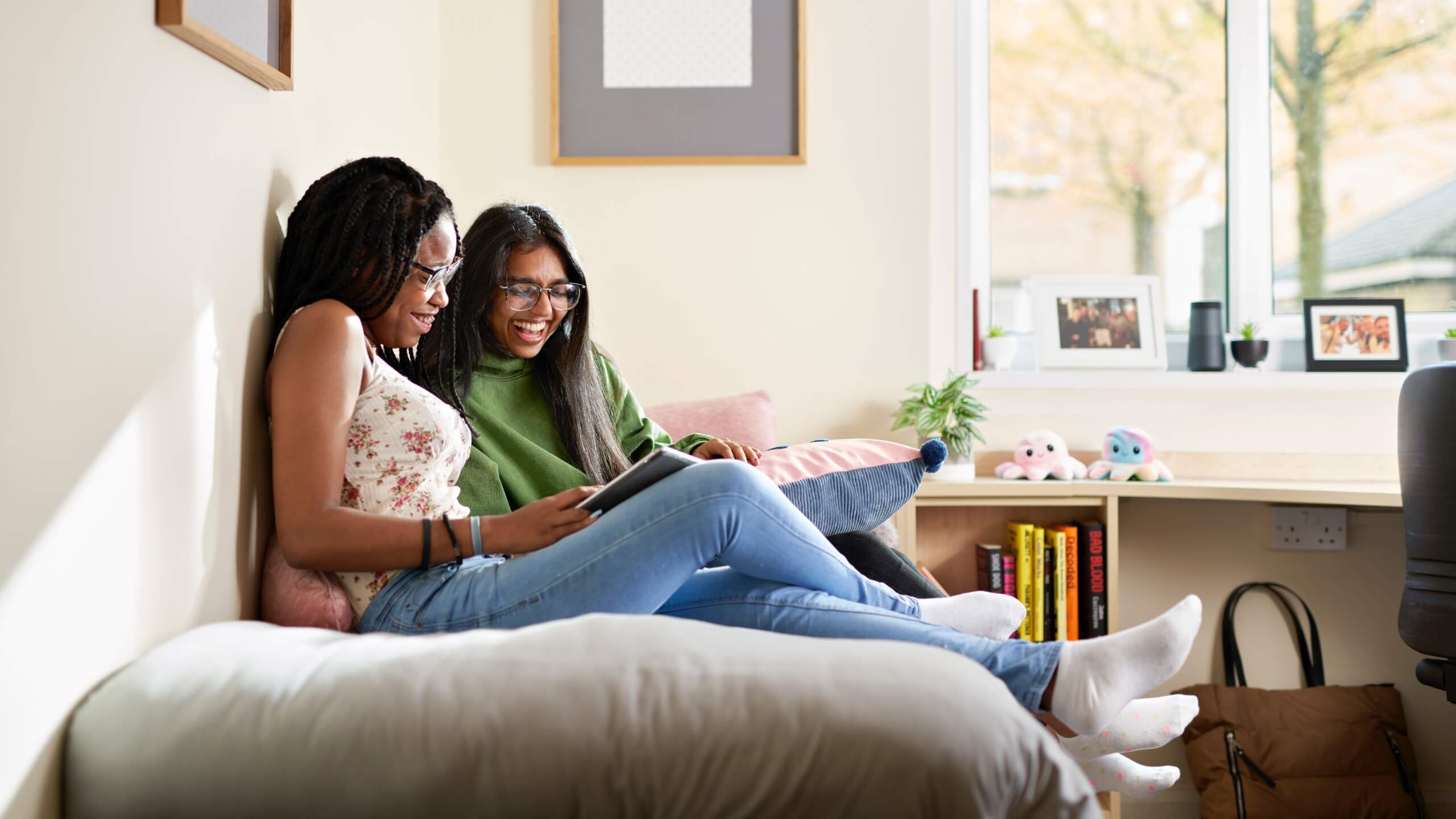 Two students sit on a bed and read.